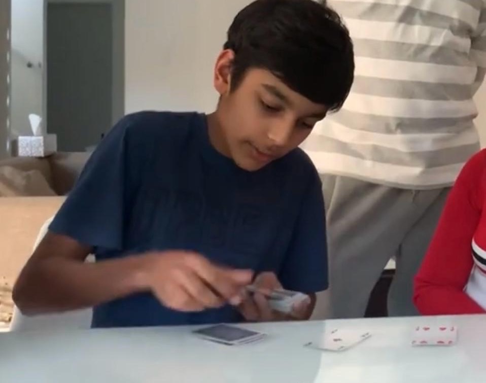 Teenage Mahir practising a card trick at the kitchen table
