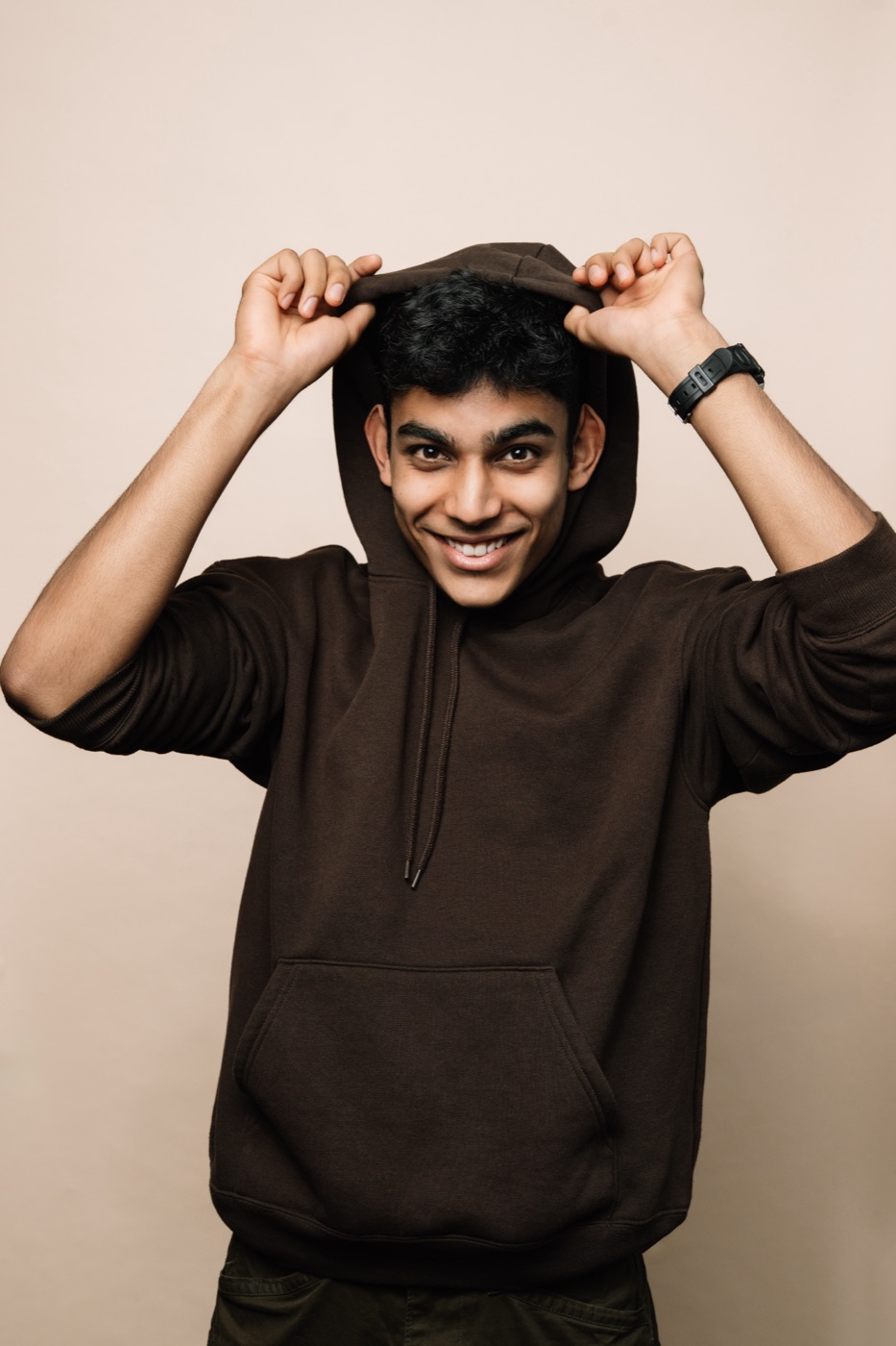 Mahir grinning in a brown hoodie, pulling the hood over his head